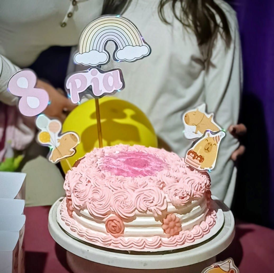 Pastel de cumpleaños escarchado en color rosa con decoraciones y adornos, incluido un arcoíris y 
