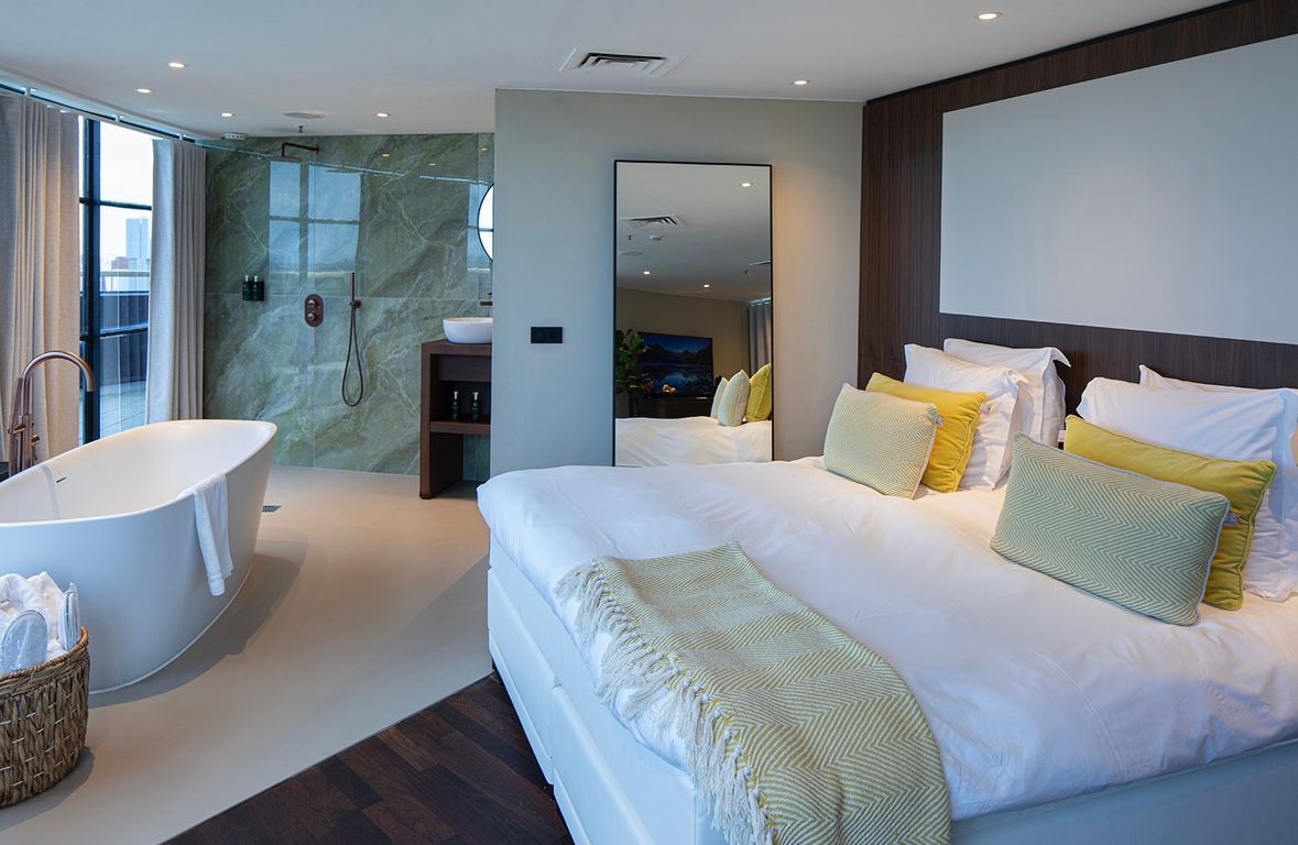 Slaapkamer met een wit bad, een groot bed met gele kussens en een grote spiegel.