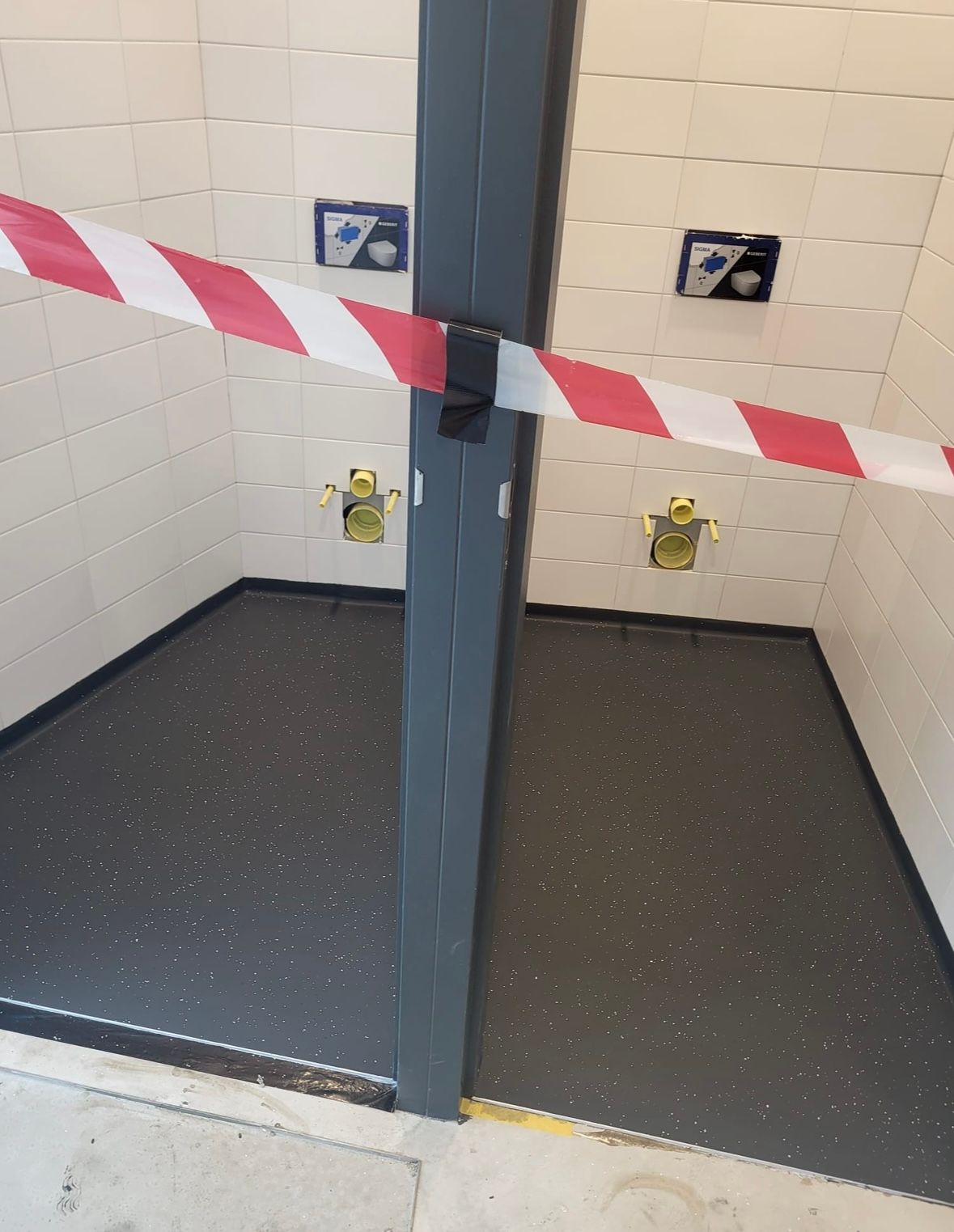 Twee douchecabines afgesloten met rood-wit afzetlint. Donkergrijze vloer, witte tegelwanden.