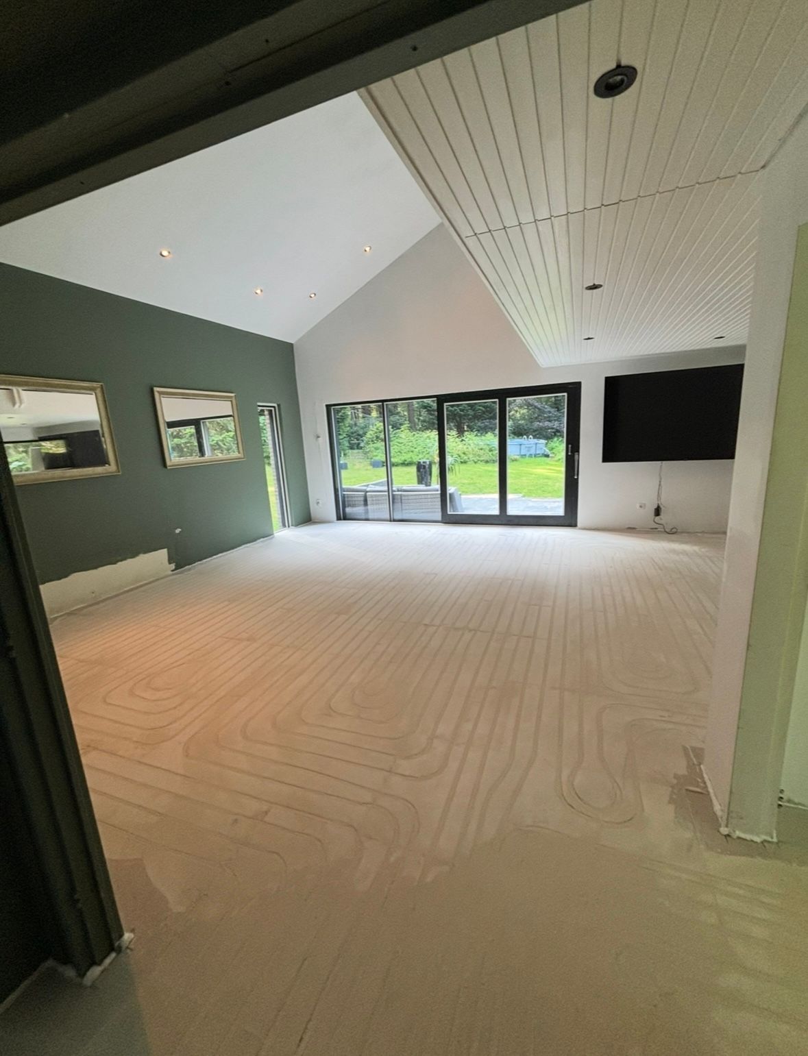 Lege woonkamer met lichtgekleurde vloer, schuifdeuren naar de achtertuin en een aan de muur gemonteerde tv.