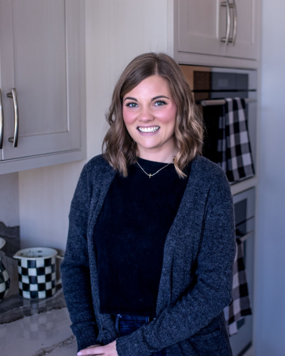 Woman smiling in a kitchen wearing a black shirt and gray cardigan.
