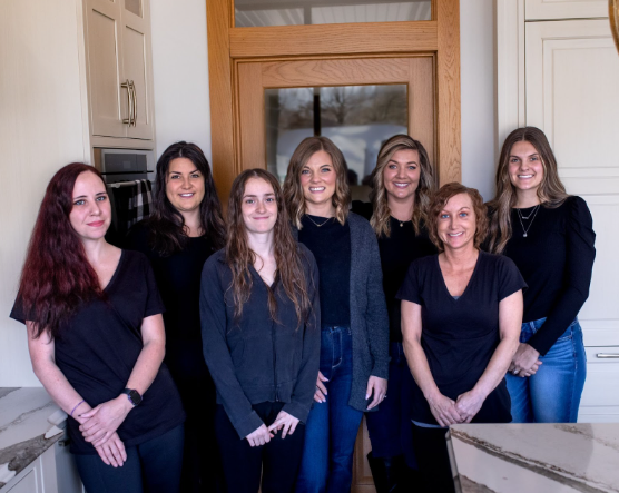 Group of seven people smiling in front of a wooden door, all wearing dark tops.
