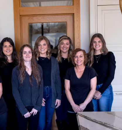 Group of seven people smiling in front of a wooden door, all wearing dark tops.