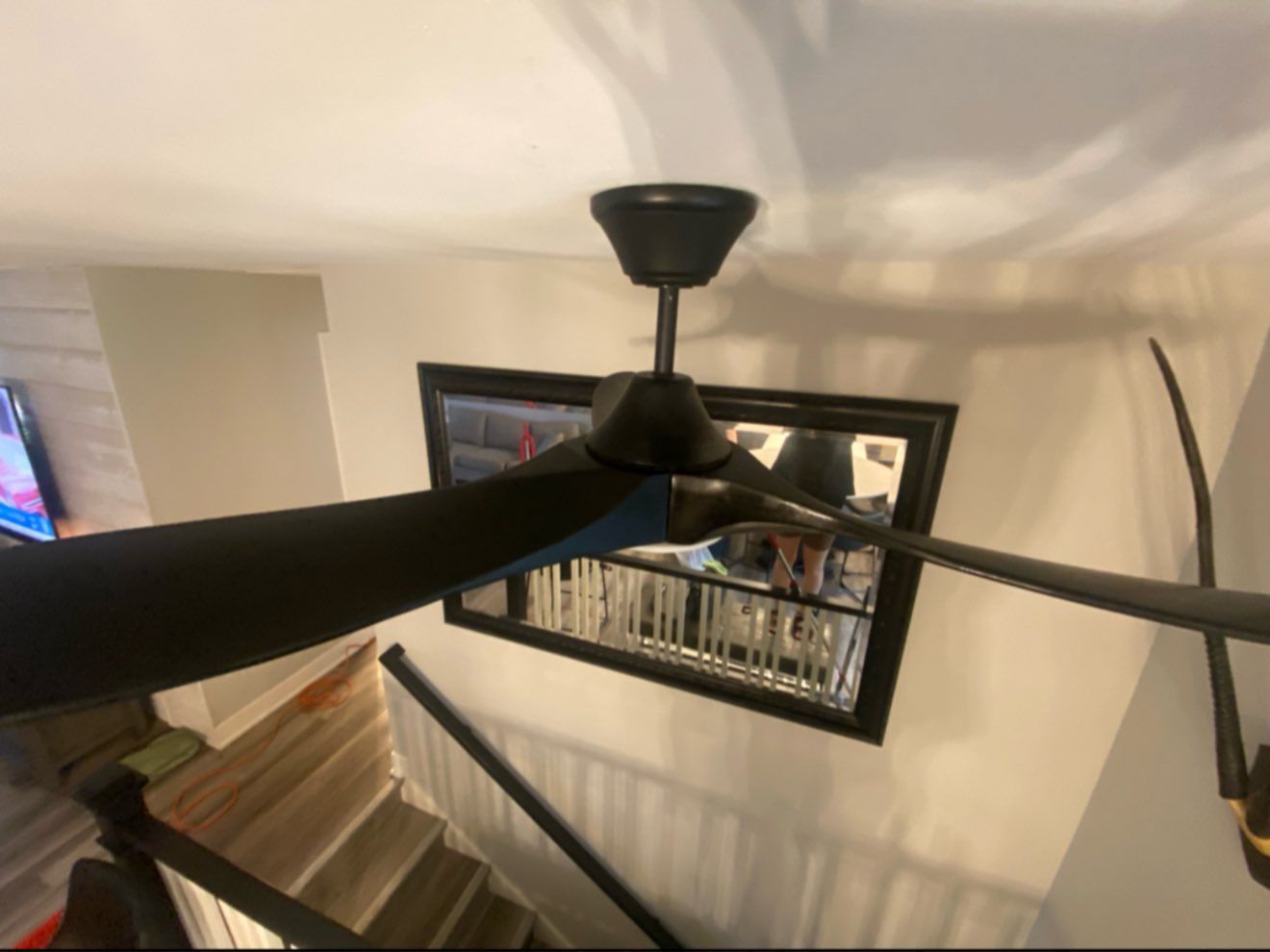 Black ceiling fan over a staircase with a black-framed mirror.
