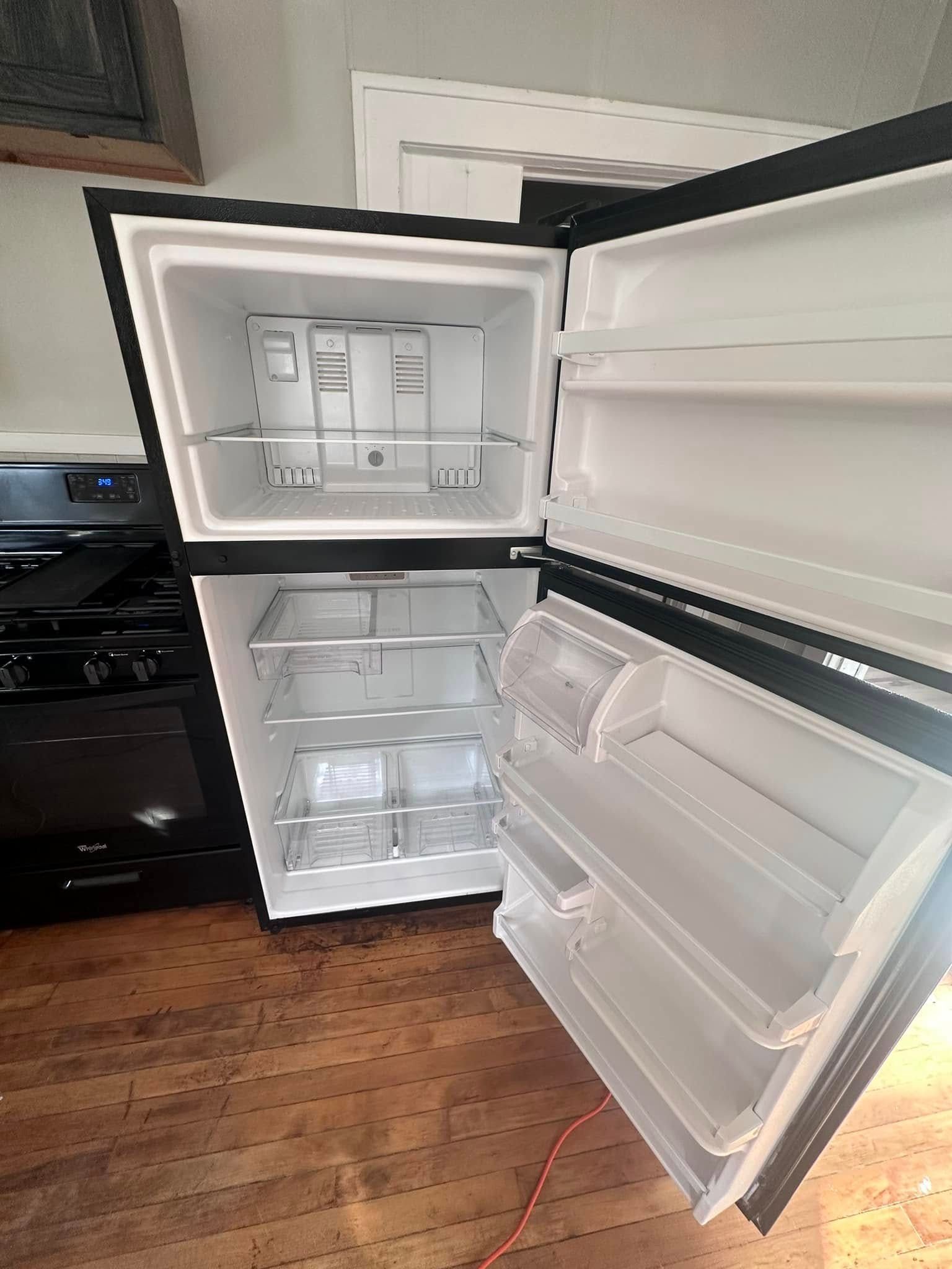 Black refrigerator with open doors, revealing interior shelves and compartments, set in a kitchen.