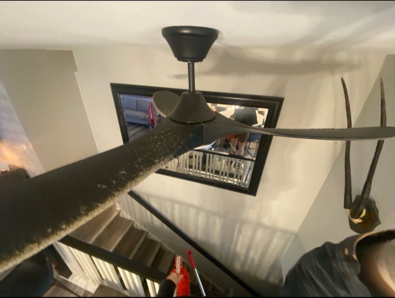 Black ceiling fan in a room with stairs and a window reflecting a room.