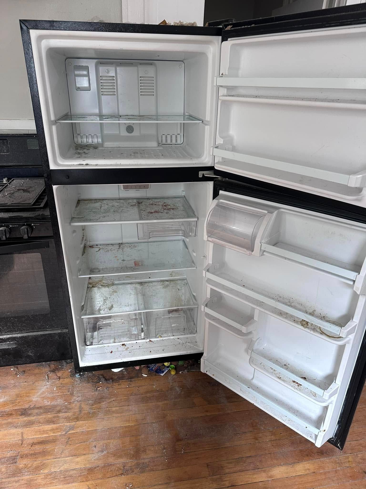 Open, dirty refrigerator with empty shelves and freezer.