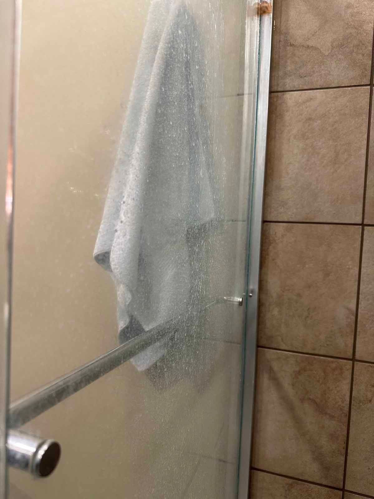 Shower door with condensation, towel hanging inside, adjacent to beige tile wall.