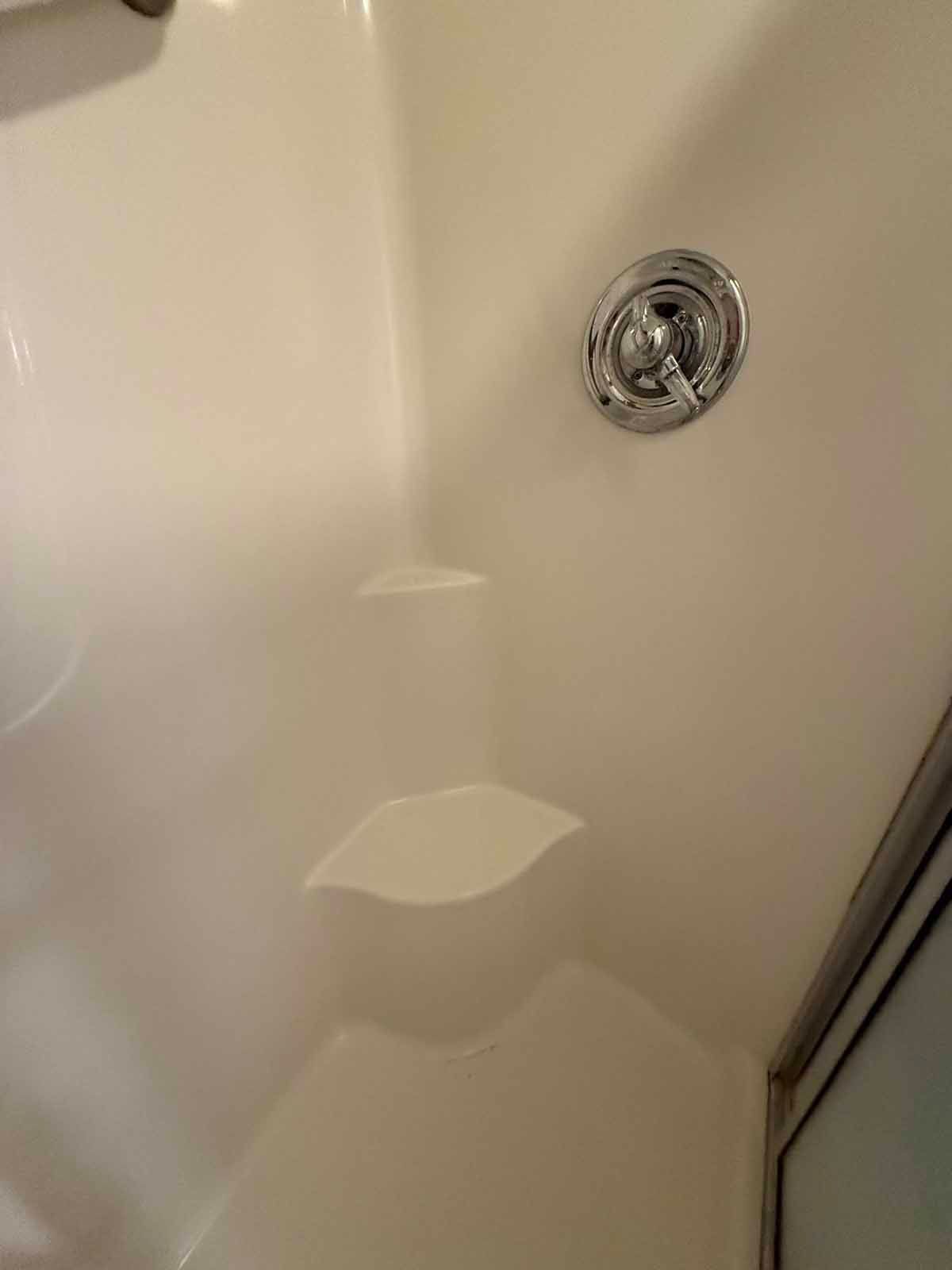 White shower stall interior with chrome faucet and built-in shelves.