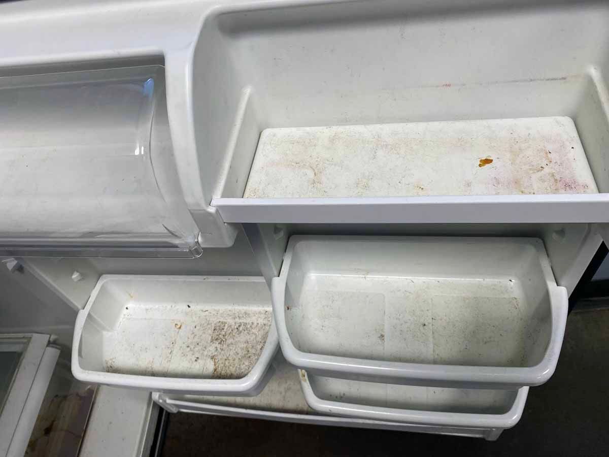Open refrigerator interior with dirty white plastic shelves and bins.