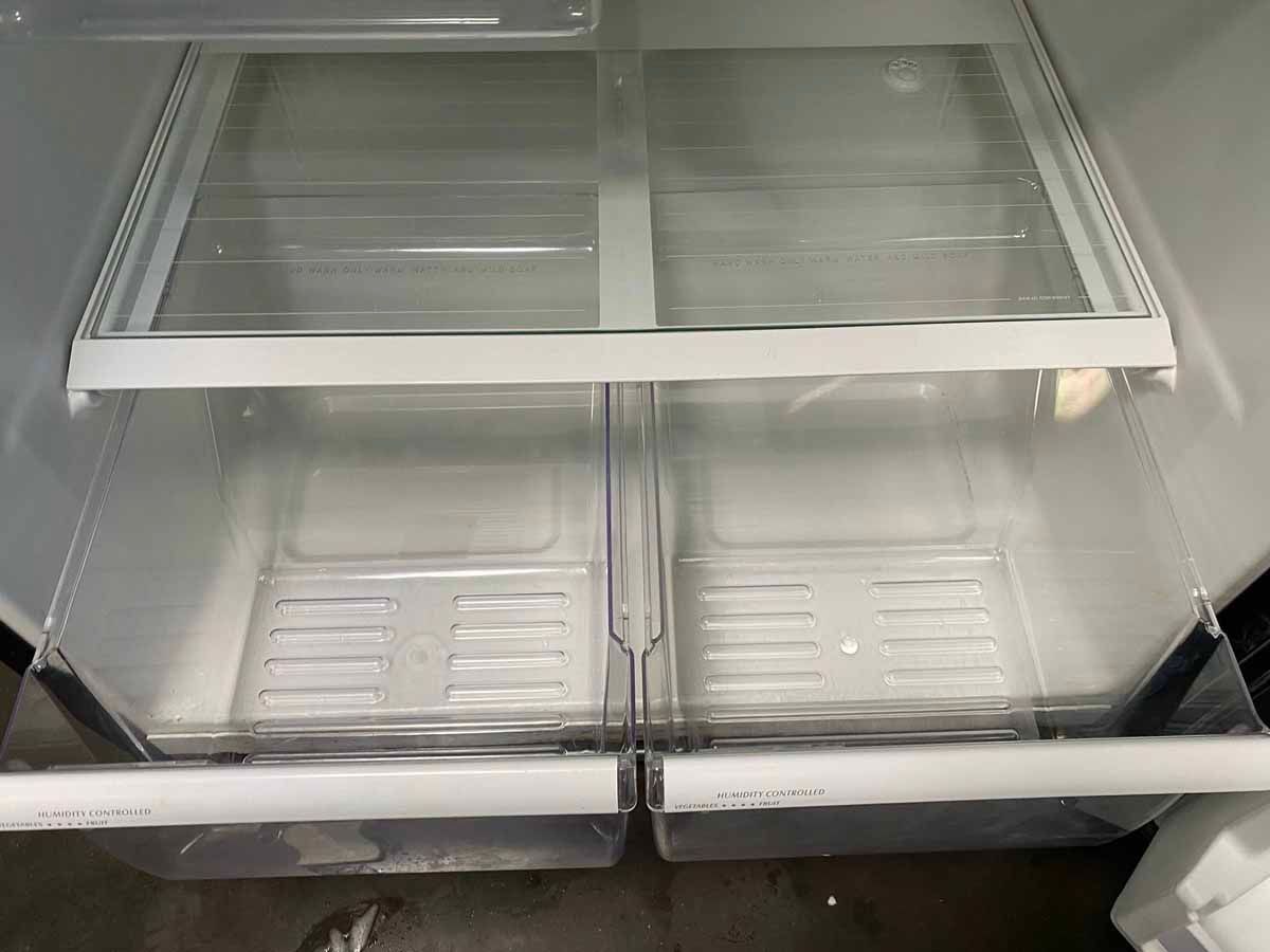 Empty refrigerator interior with glass shelves and drawers.