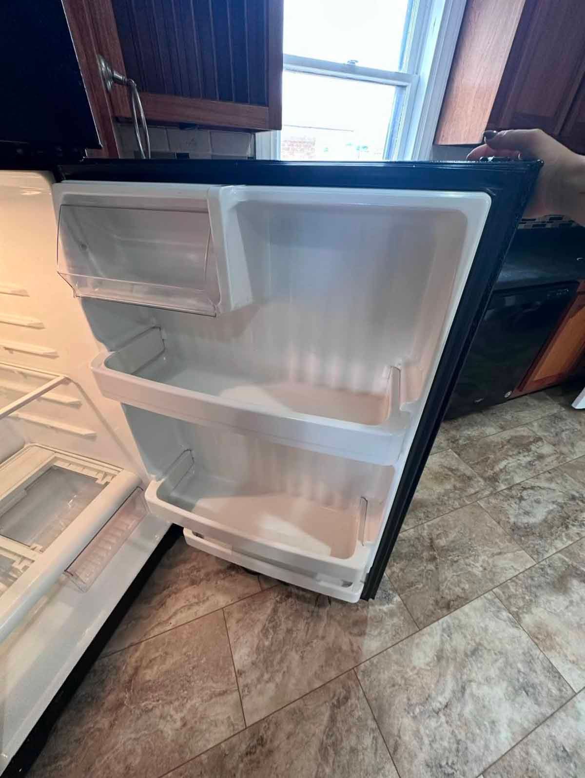 A small, open black refrigerator with white interior shelves and a clear crisper drawer, indoors.