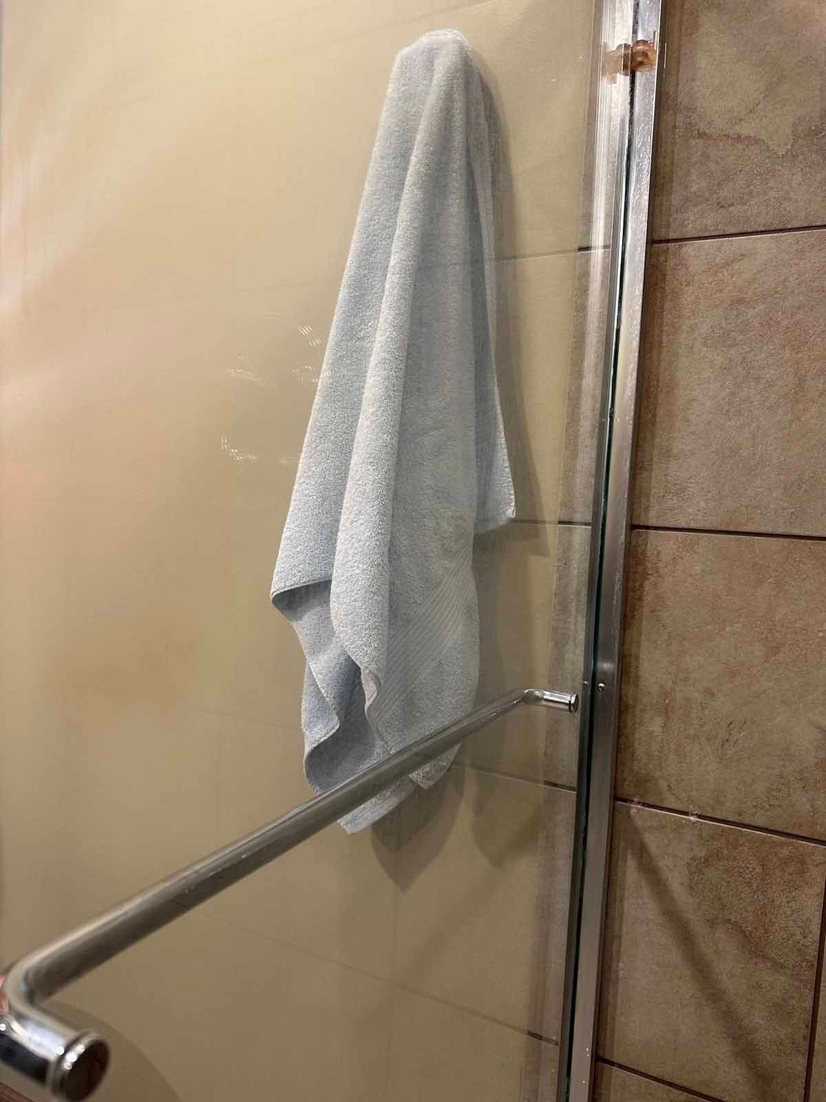 A light blue towel hangs from a chrome shower door handle next to a stone wall.