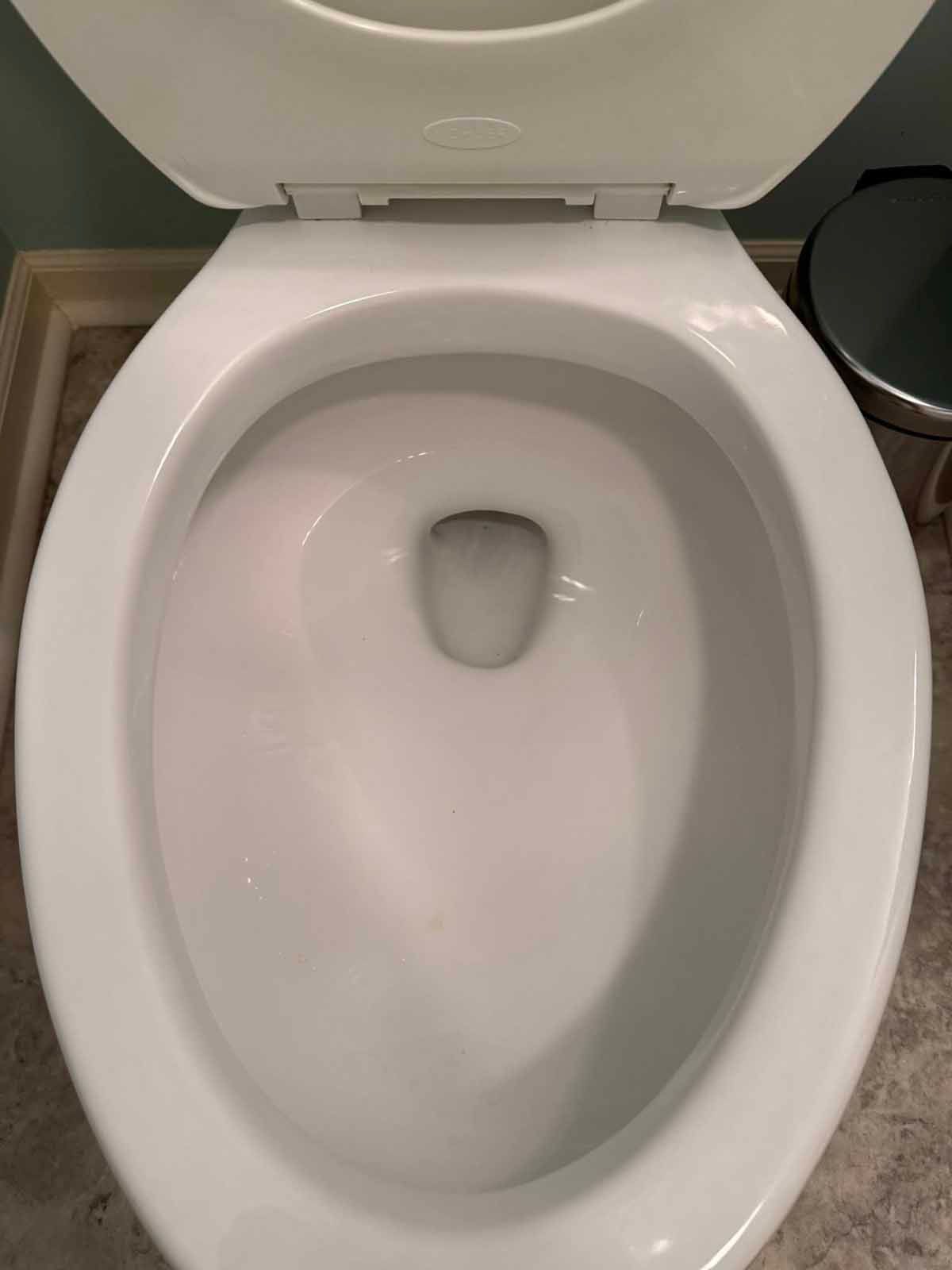 A white toilet bowl with the seat up, inside a bathroom.