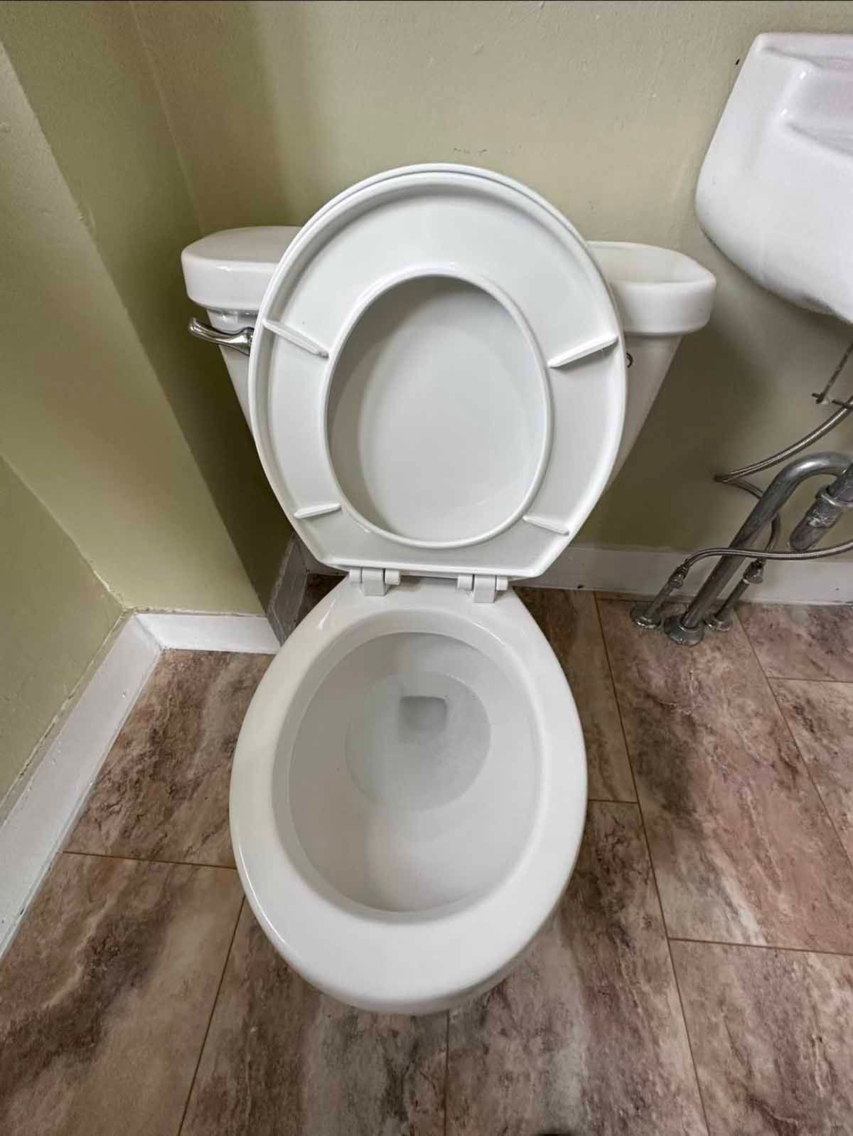White toilet with the lid up in a bathroom; tan and brown patterned flooring, light green wall.