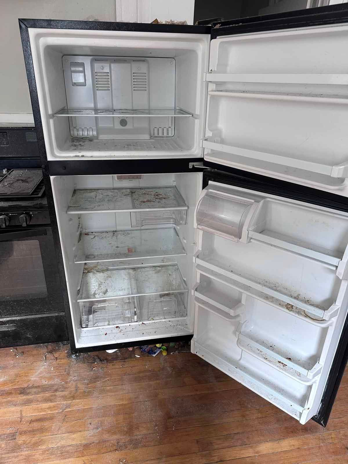A dirty, open refrigerator in a kitchen with a gas stove and wooden floor.