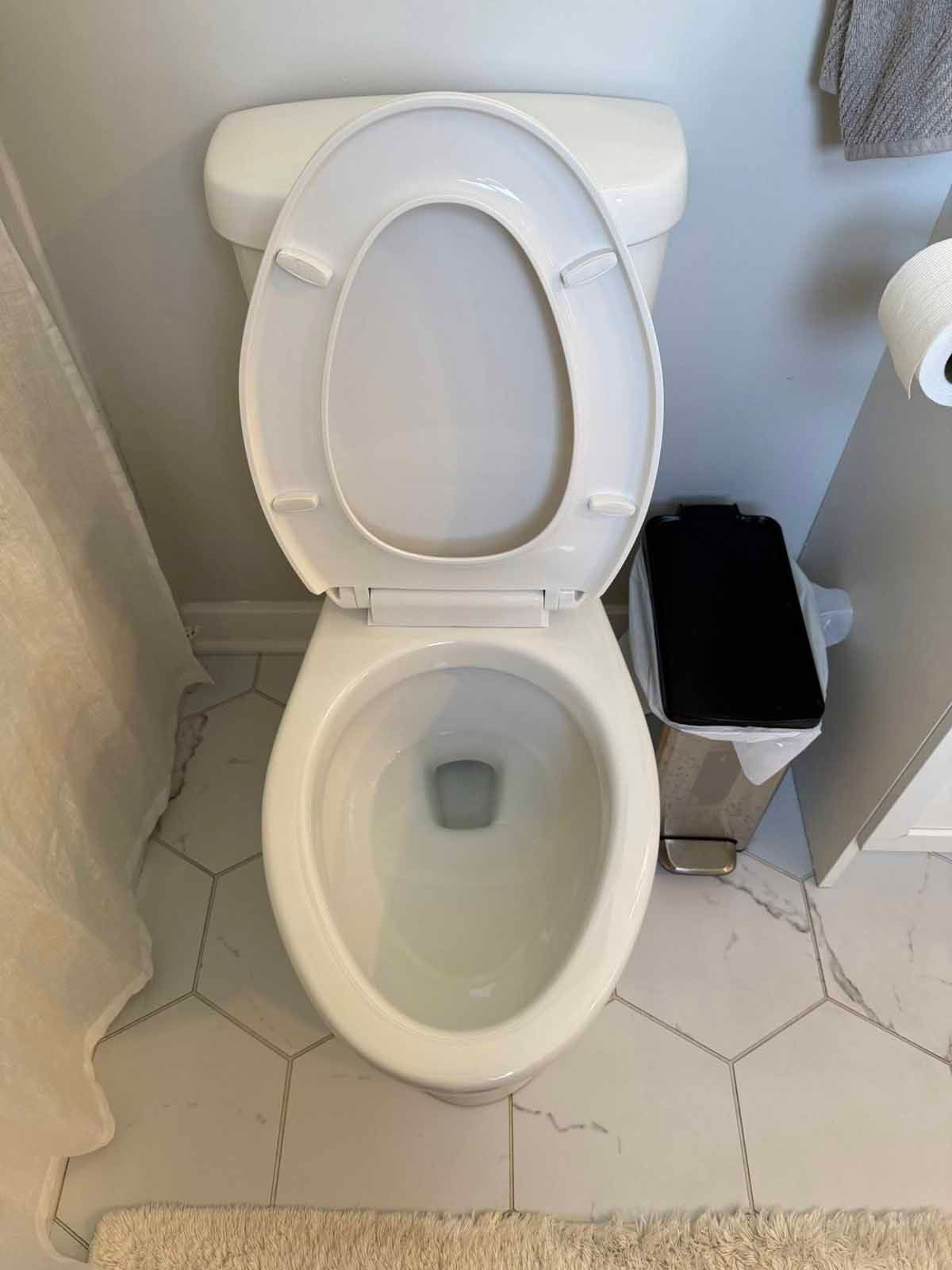 Open toilet seat, white ceramic, in bathroom with gray walls and hexagonal tile floor.