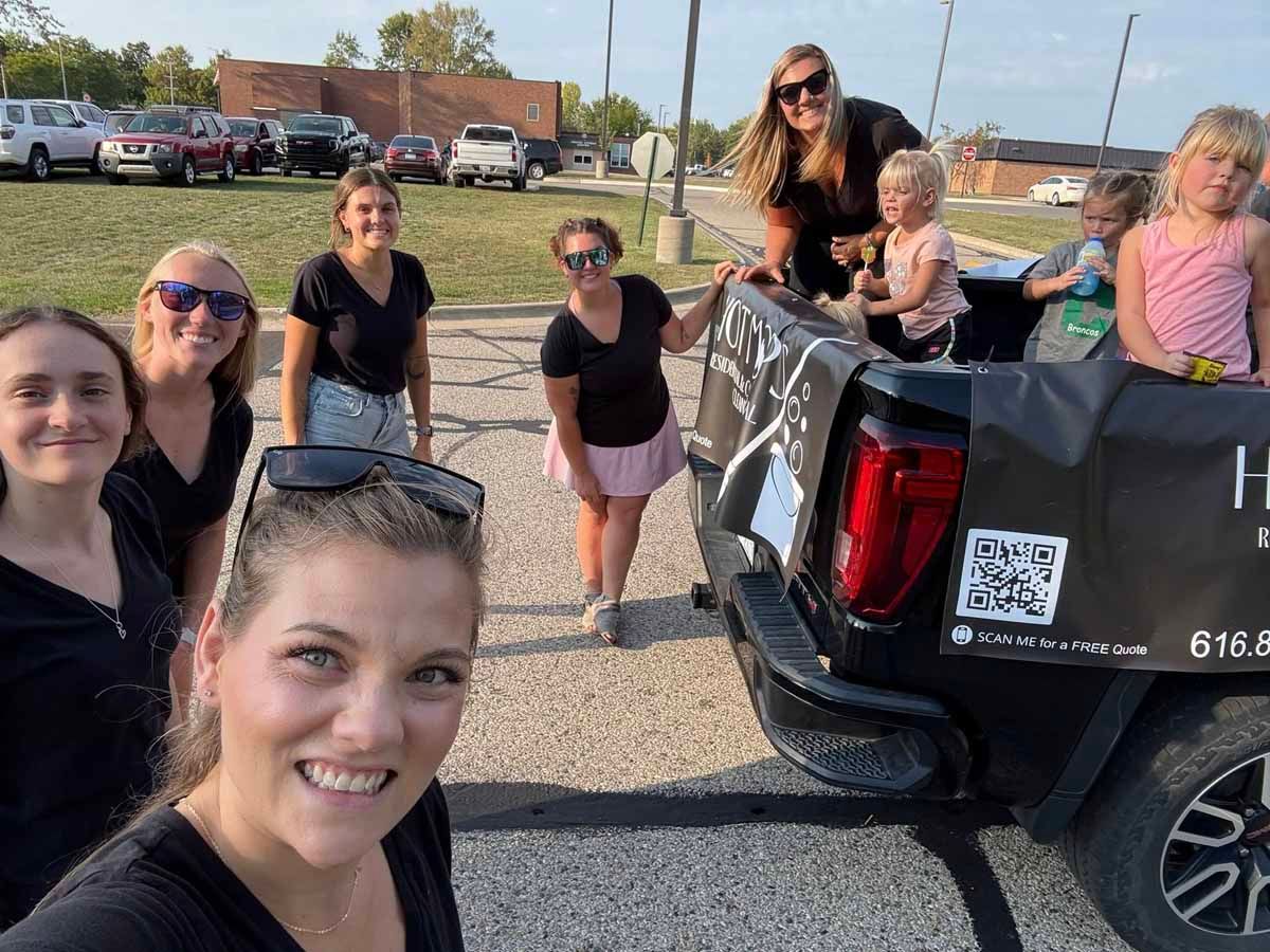Group of women posing in a kitchen. Some are sitting and standing, all in dark clothing.