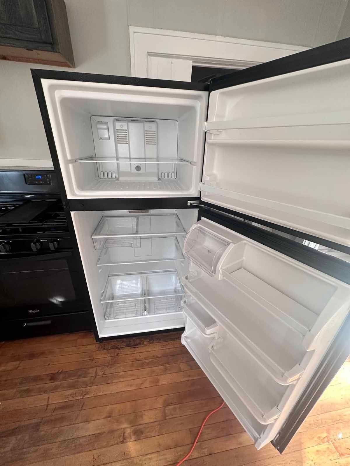 Black refrigerator with open doors, revealing shelves. Located next to a stove.