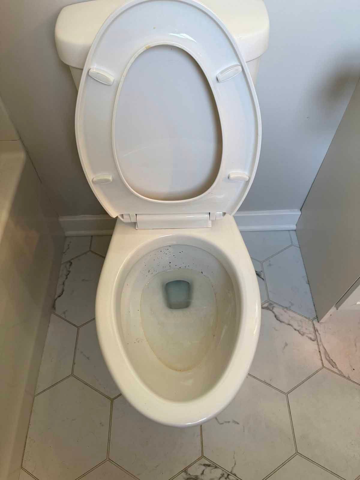 Toilet with open lid, white ceramic, centered on hexagonal patterned floor.