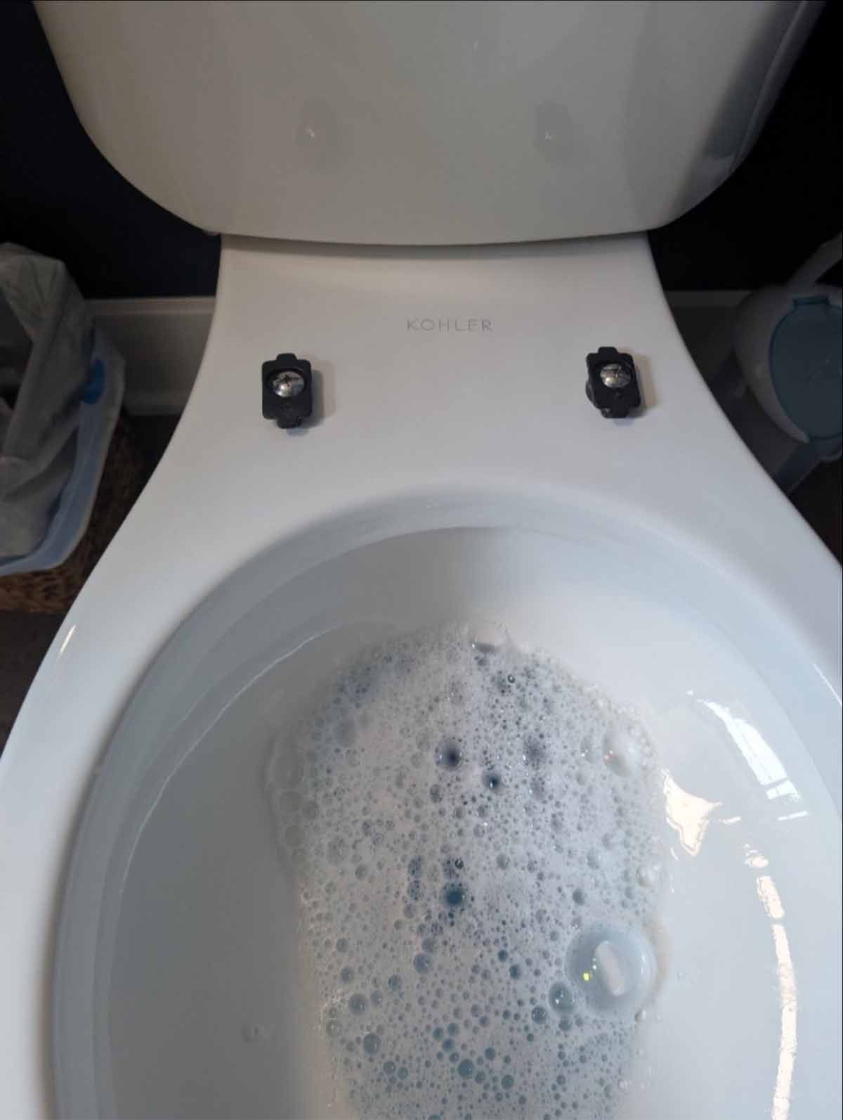 Top-down view of a white toilet bowl with soapy water and black hinge caps.