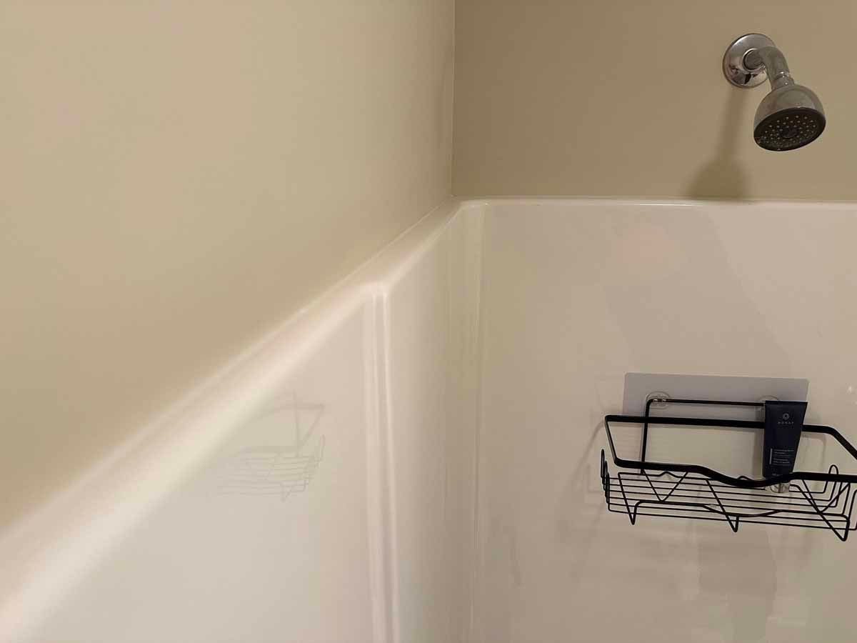 Corner of a shower with a shower head, toiletries basket, and beige walls.