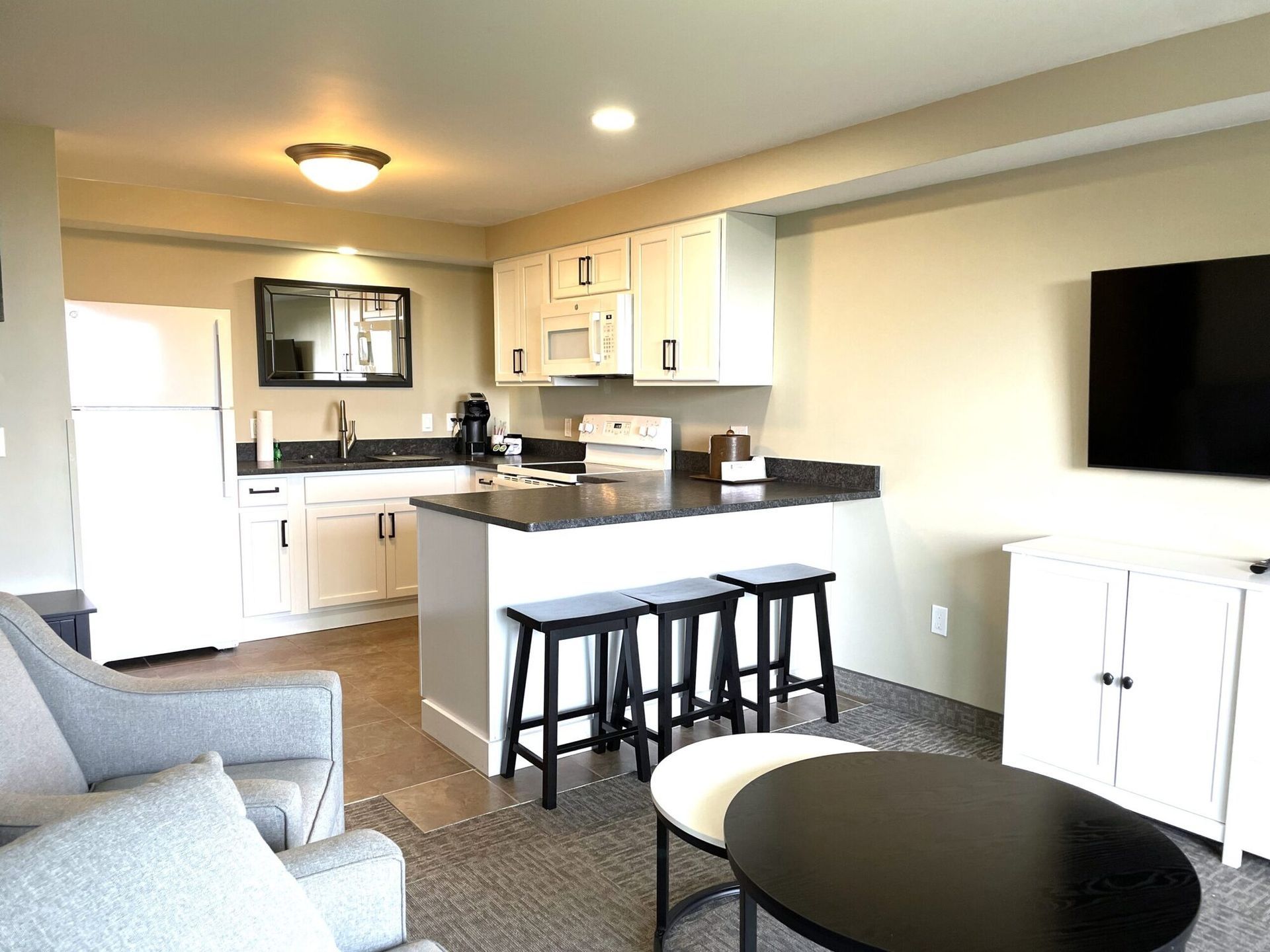 A living room with a kitchen and a flat screen tv.
