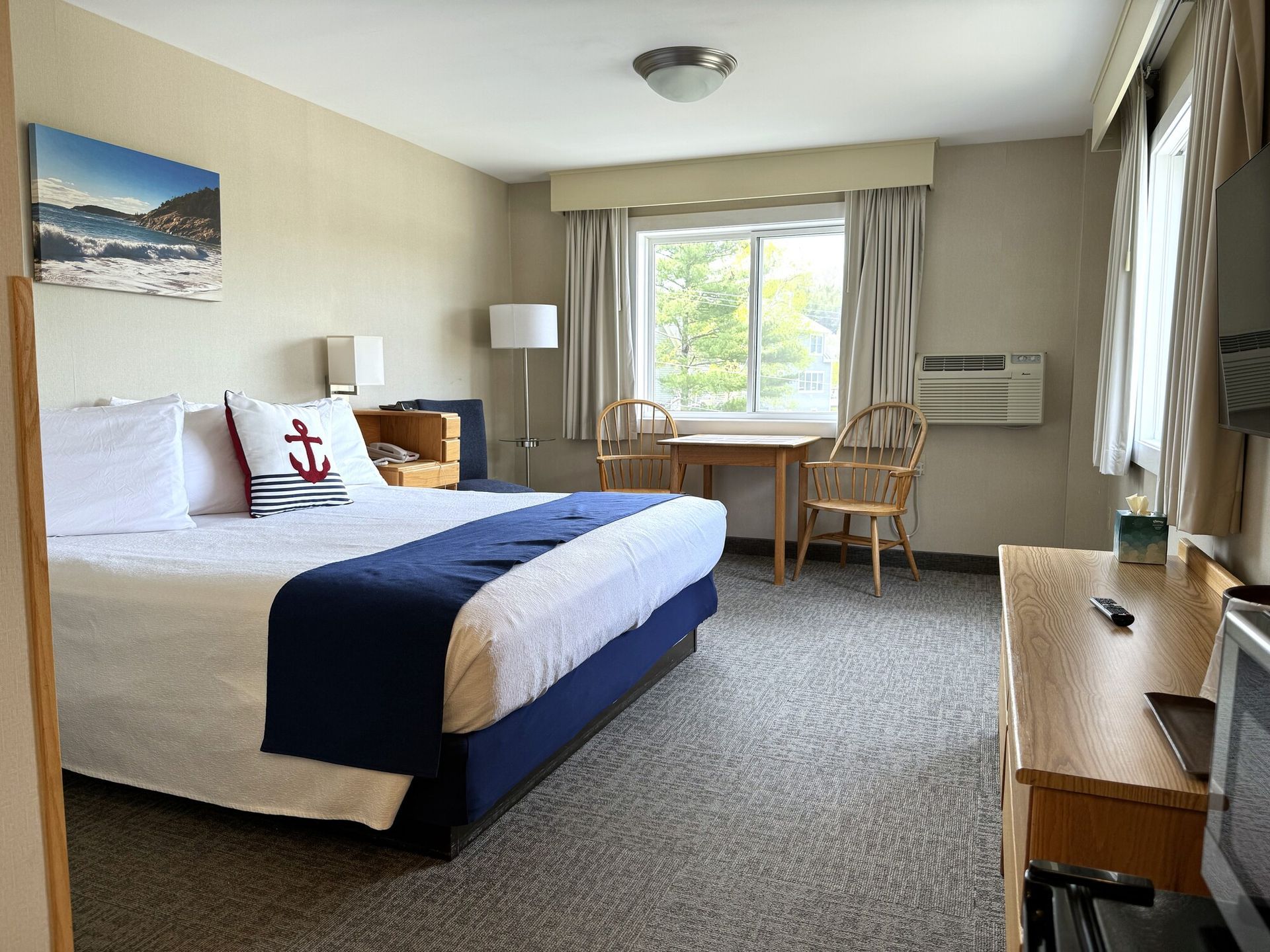 A hotel room with a king size bed , desk , chair and television.