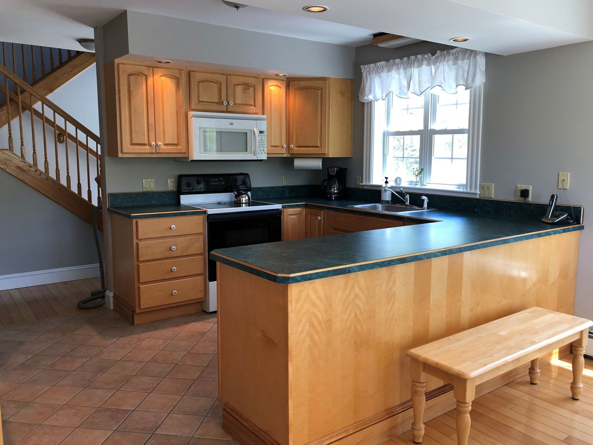 A kitchen with wooden cabinets , a stove , a microwave , a sink , and a bench.