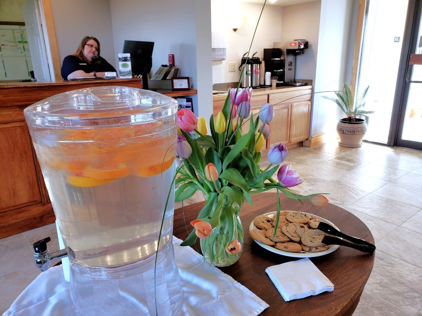 A pitcher of water sits on a table next to a vase of flowers and a plate of cookies.