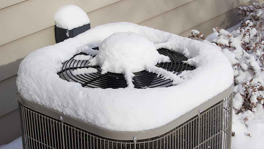 Air conditioning unit covered in snow outside a building.
