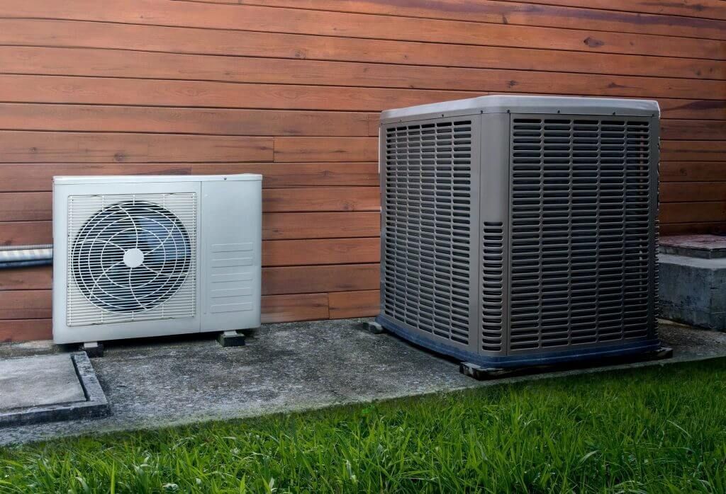 Two air conditioners are sitting next to each other on the side of a building.