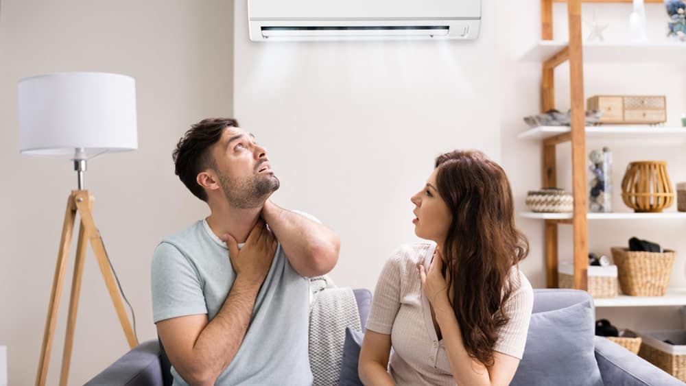 Man and woman sitting on couch sweating due to poor ac air flow