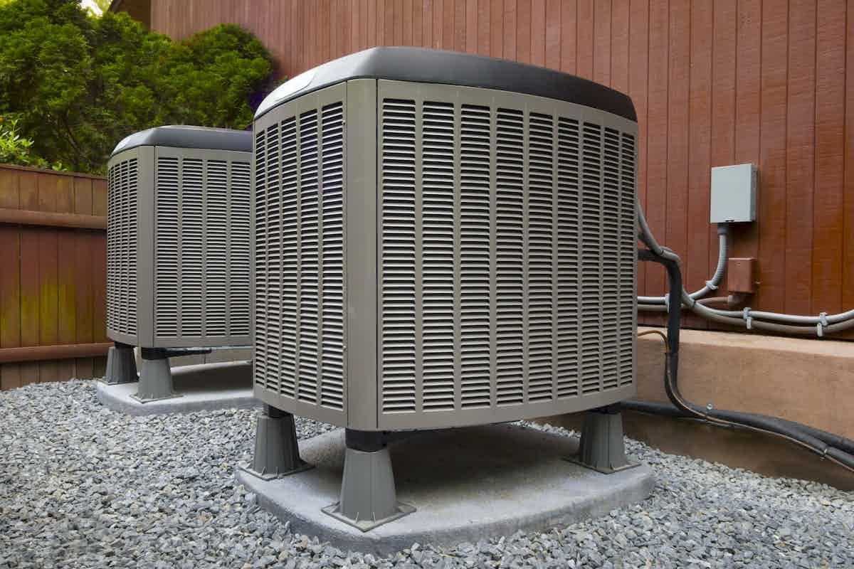 two air conditioners are sitting on gravel outside of a house .
