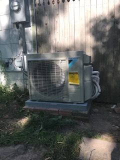 An air conditioner is sitting outside of a house next to a wooden fence.