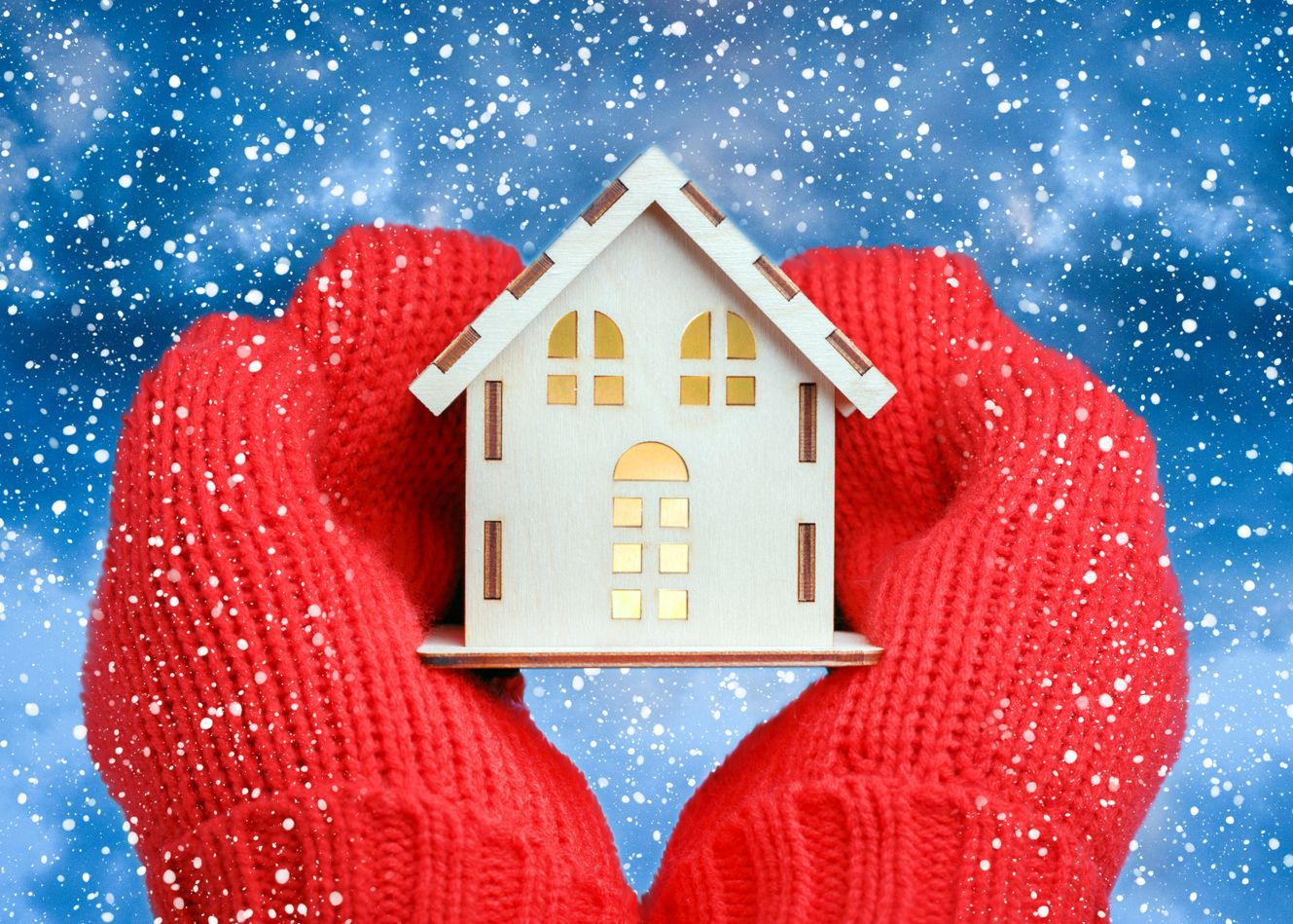 A person wearing red gloves is holding a small wooden house.