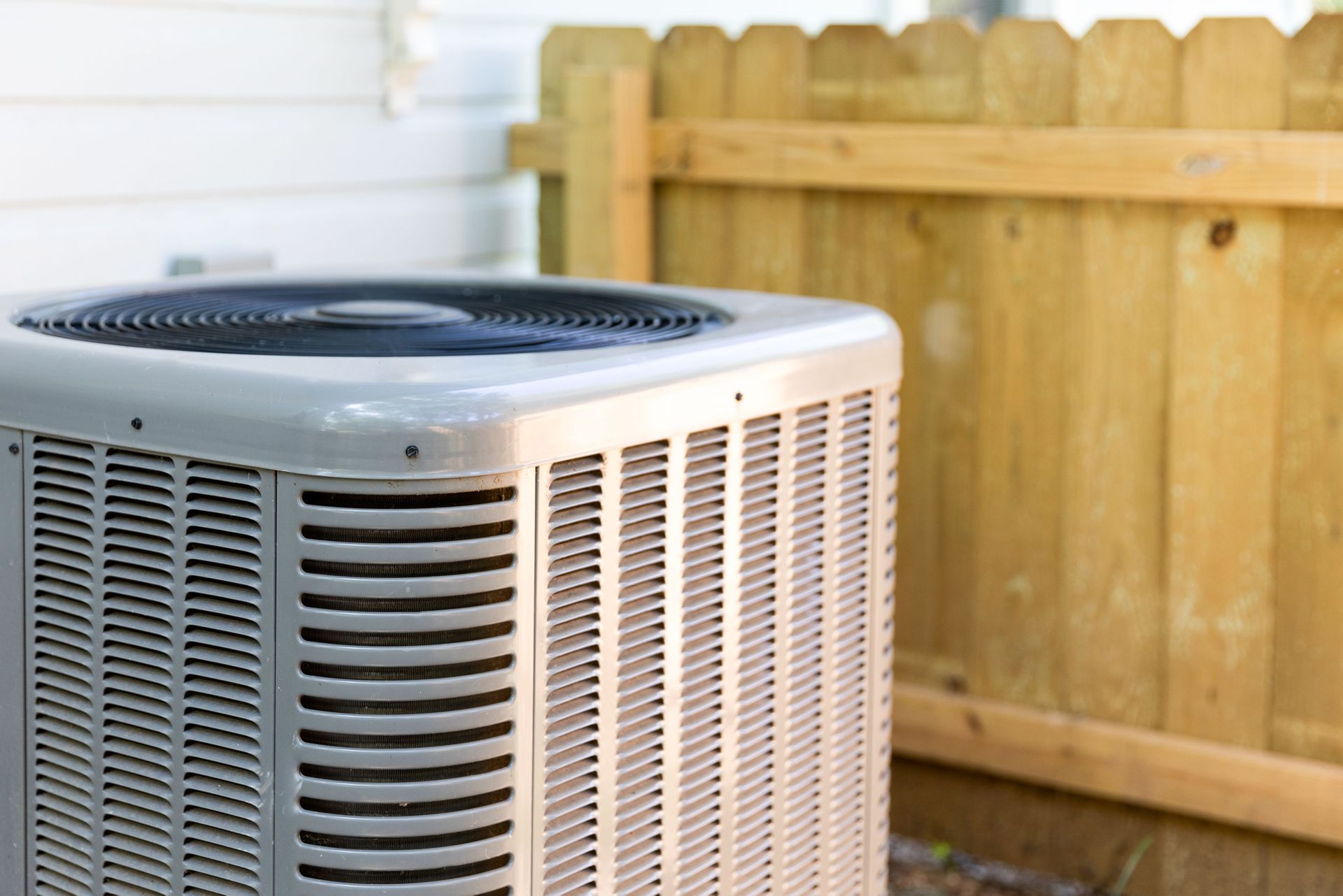 An air conditioner is sitting in front of a wooden fence.