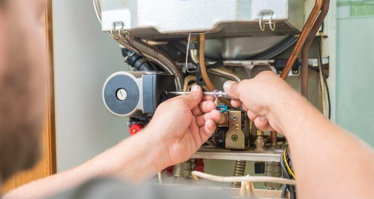 A man is fixing a boiler with a screwdriver.