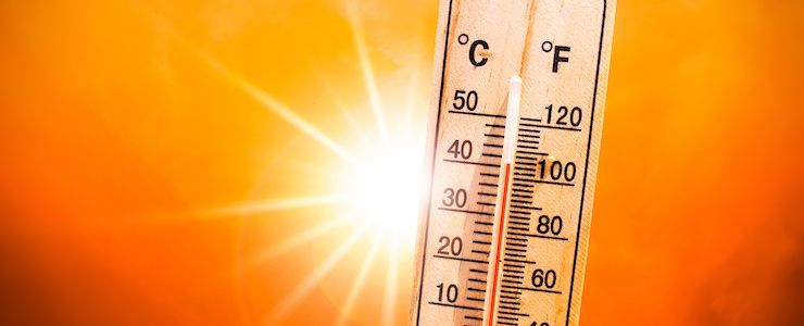 A thermometer with a bright sun shining behind it. The temperature is high on the scale.