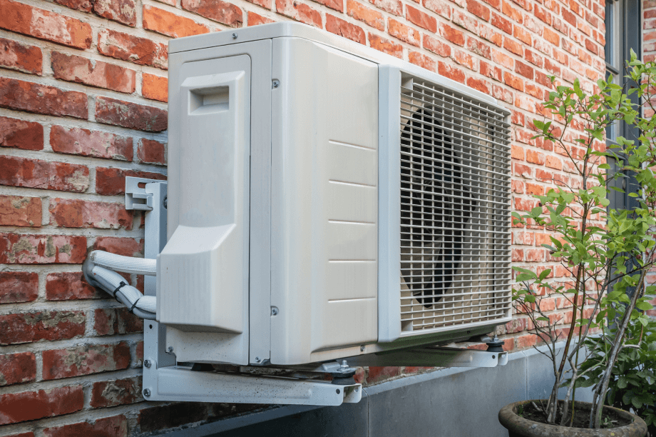 A white air conditioner is mounted on the side of a brick building.