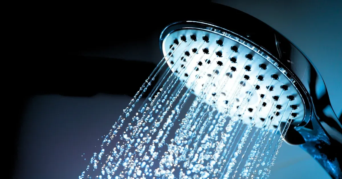 Chrome shower head with water spraying against a dark blue background.