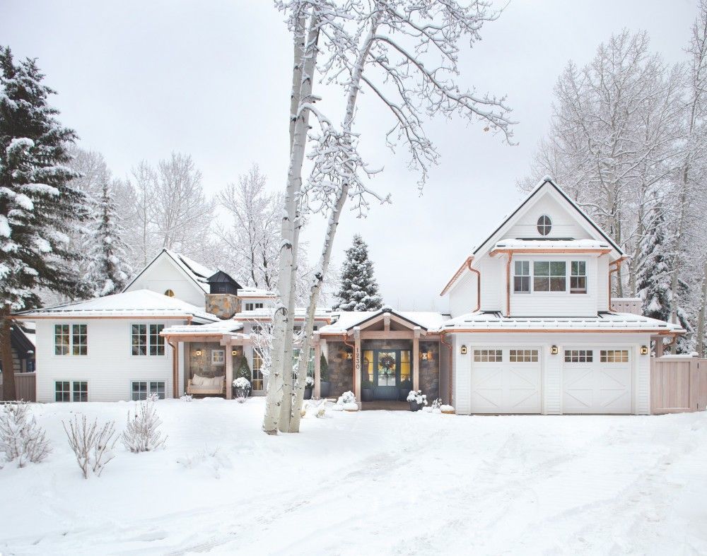 A large white house is surrounded by snow and trees