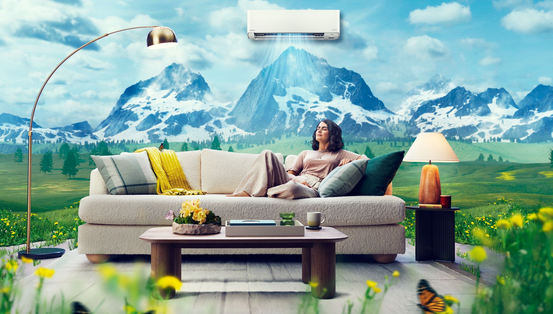 A woman is sitting on a couch in a living room with mountains in the background.