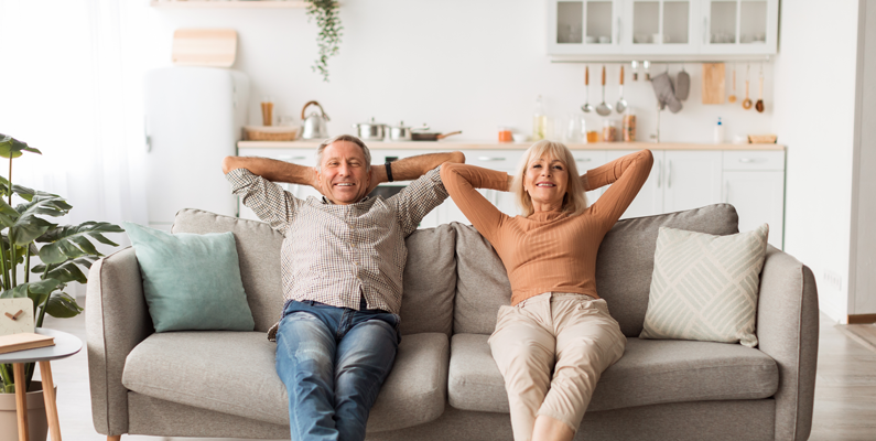 A man and a woman are sitting on a couch with their hands behind their heads.