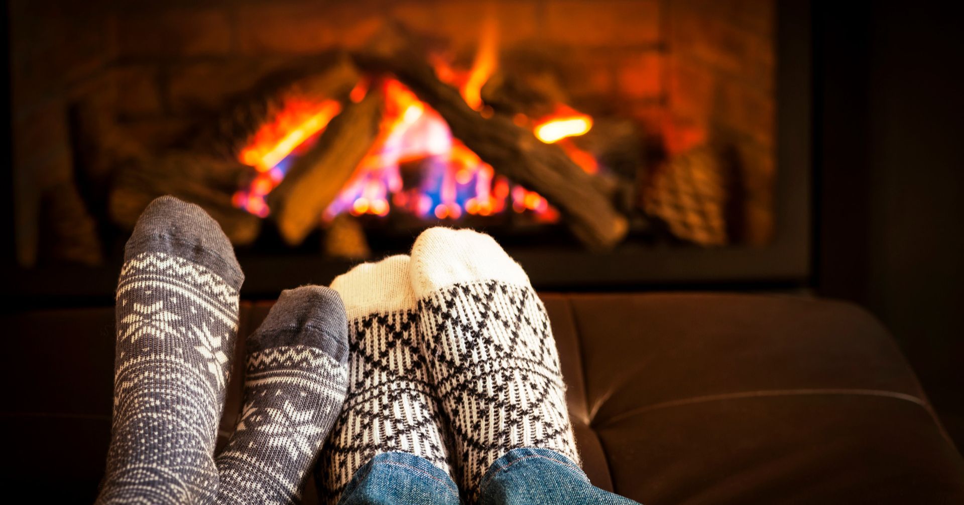 Feet in cozy patterned socks in front of a fireplace with burning flames.