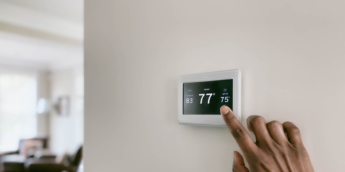 persons hand adjusting digital thermostat on wall