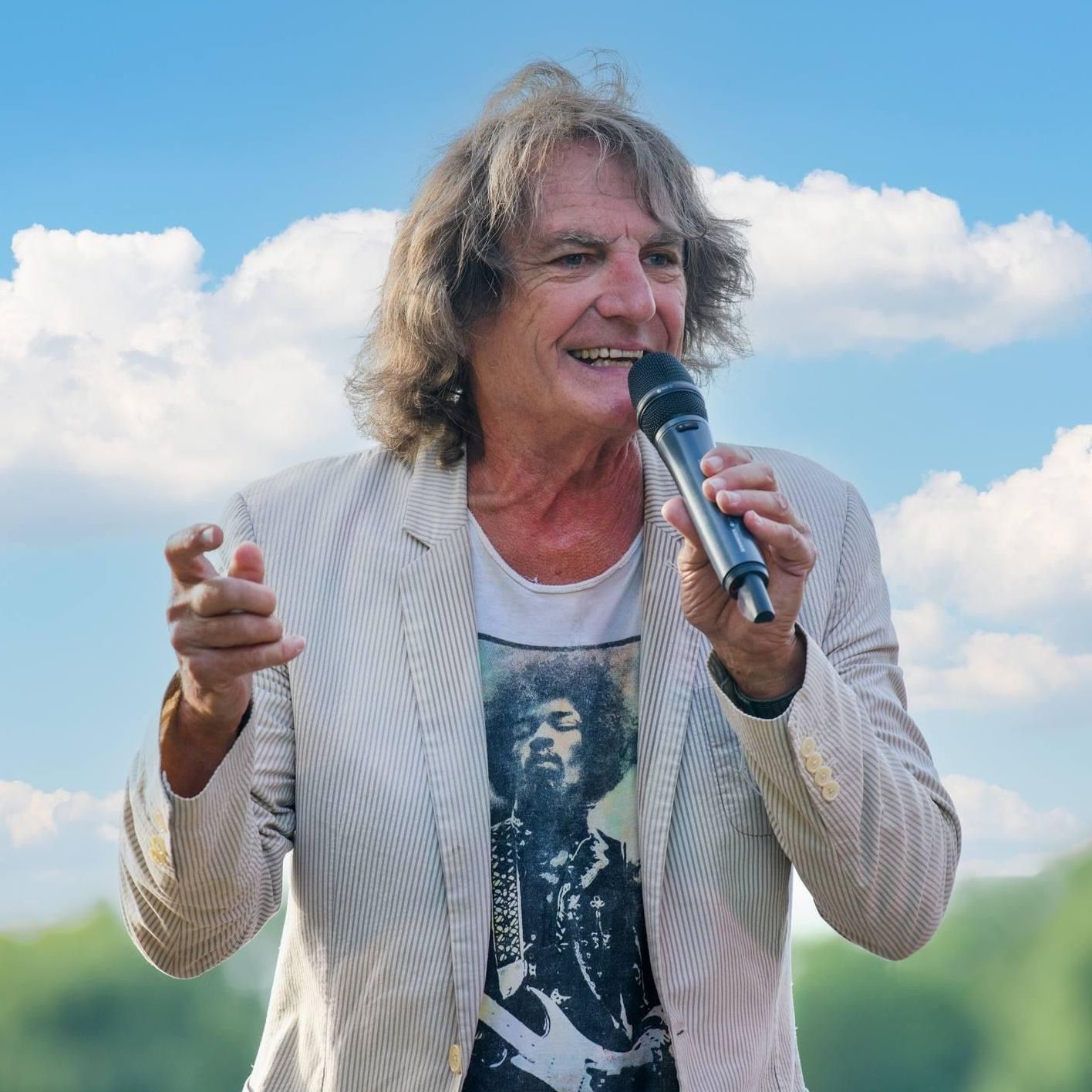 A man is singing into a microphone while wearing a jimi hendrix shirt