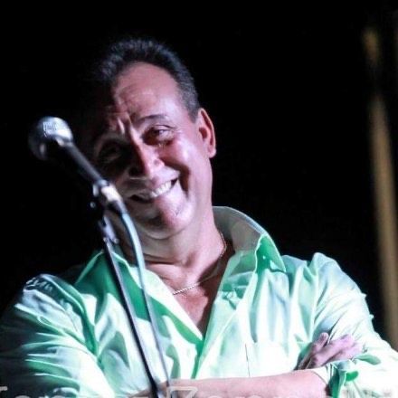 A man in a green shirt is smiling in front of a microphone