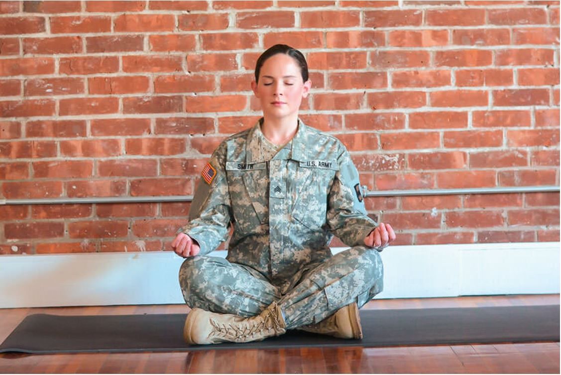 A woman in a military uniform is meditating on a yoga mat.