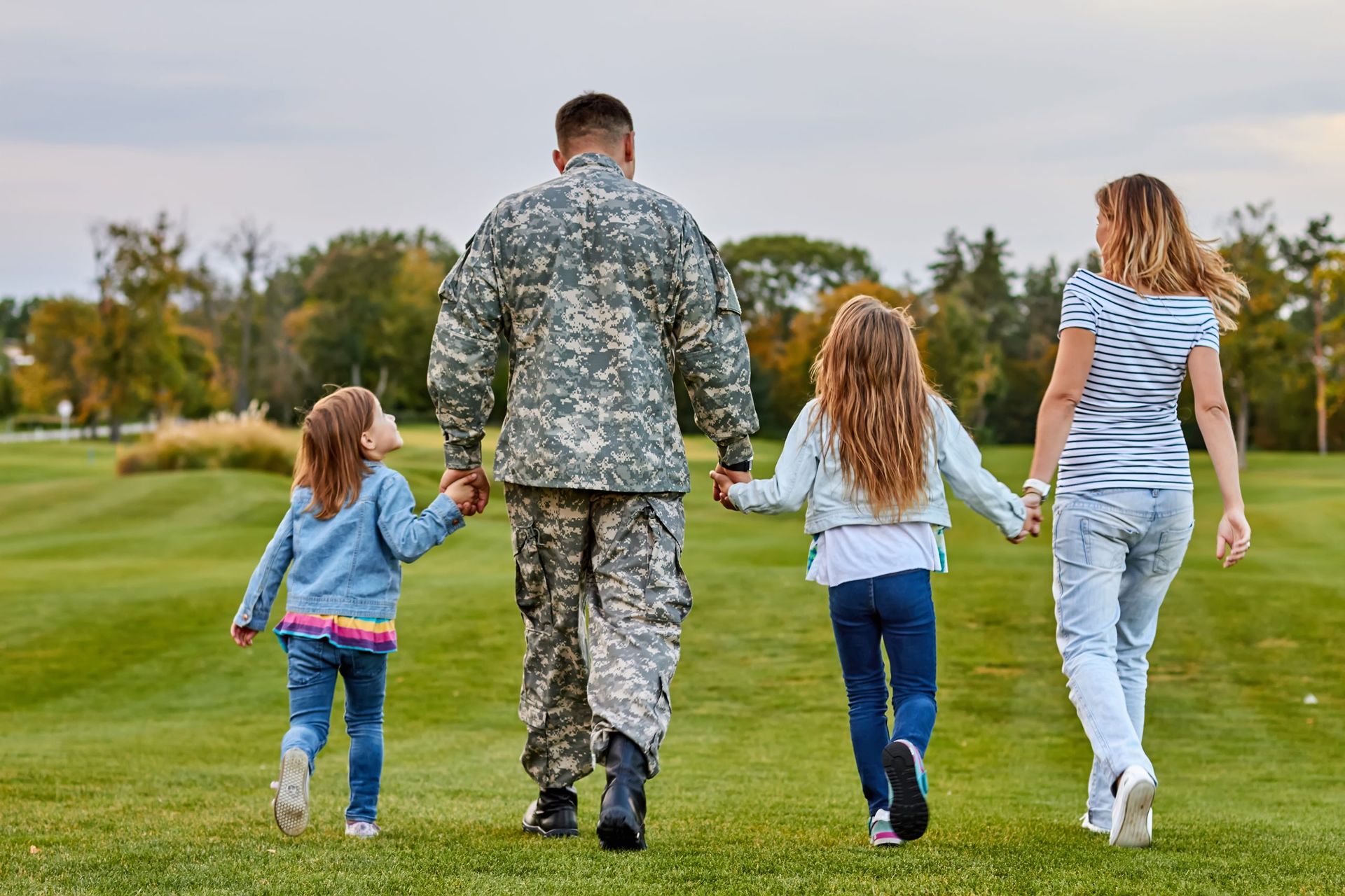 Family walking away across a grassy field, holding hands on a cloudy day